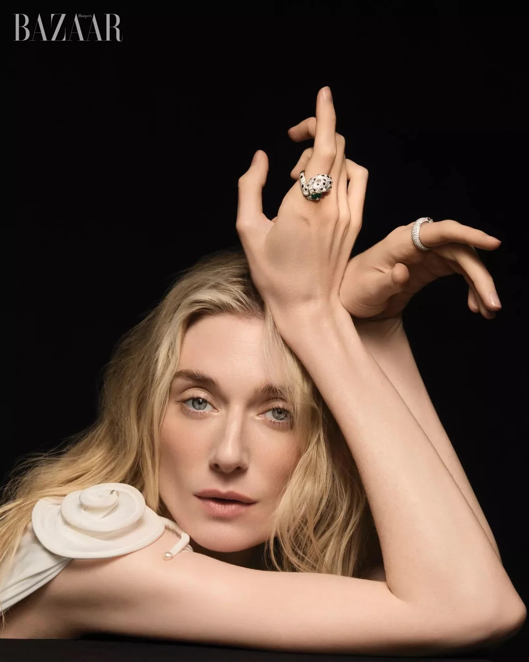 Elizabeth Debicki posing against a black background wearing statement rings and a white sculptural top for Harper's Bazaar Australia.