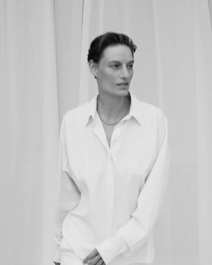 Veronika Kunz posing in an oversized white button-down collared shirt with draped fabric in the background.