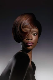 Portrait of a Black woman model with sculpted brown hair and glossy pink lips against a dark gradient background