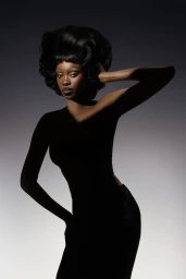 Black woman with voluminous dark hairstyle and vibrant green eyeshadow posing against a gradient grey studio backdrop