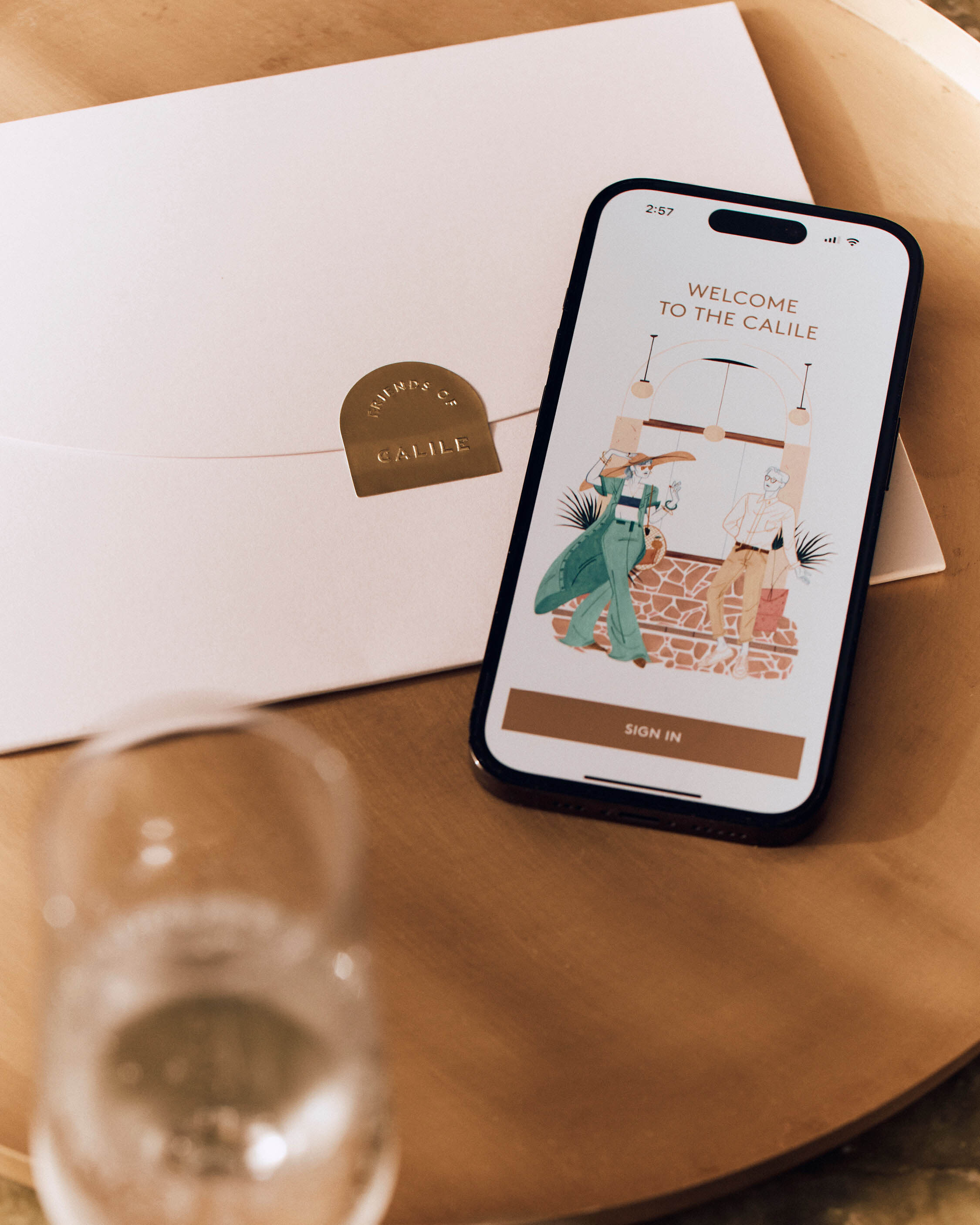 Smartphone displaying a hotel app interface next to a white envelope with a gold seal on a wooden table.