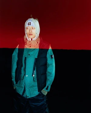 Model Li Cheng Yuan wearing a hooded teal technical jacket and black puffer vest against a split red and black background.