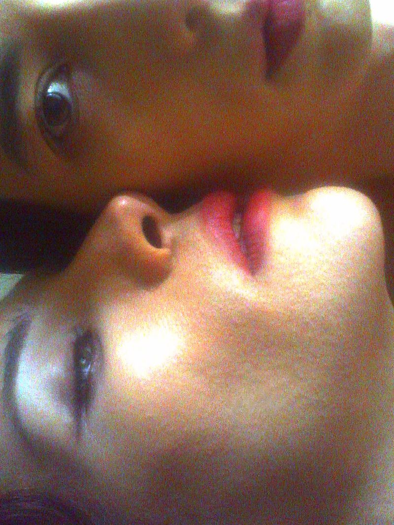 Extreme close-up portrait of two faces positioned head to head with warm lighting, soft focus, and visible film grain.