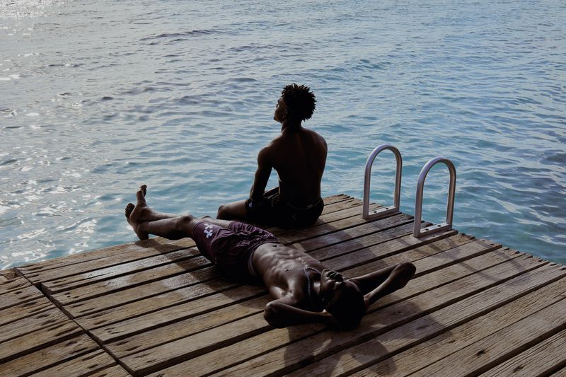 Two black men relaxing on a wooden dock by the ocean for Conde Nast Traveler Spain by Abel Trujillo