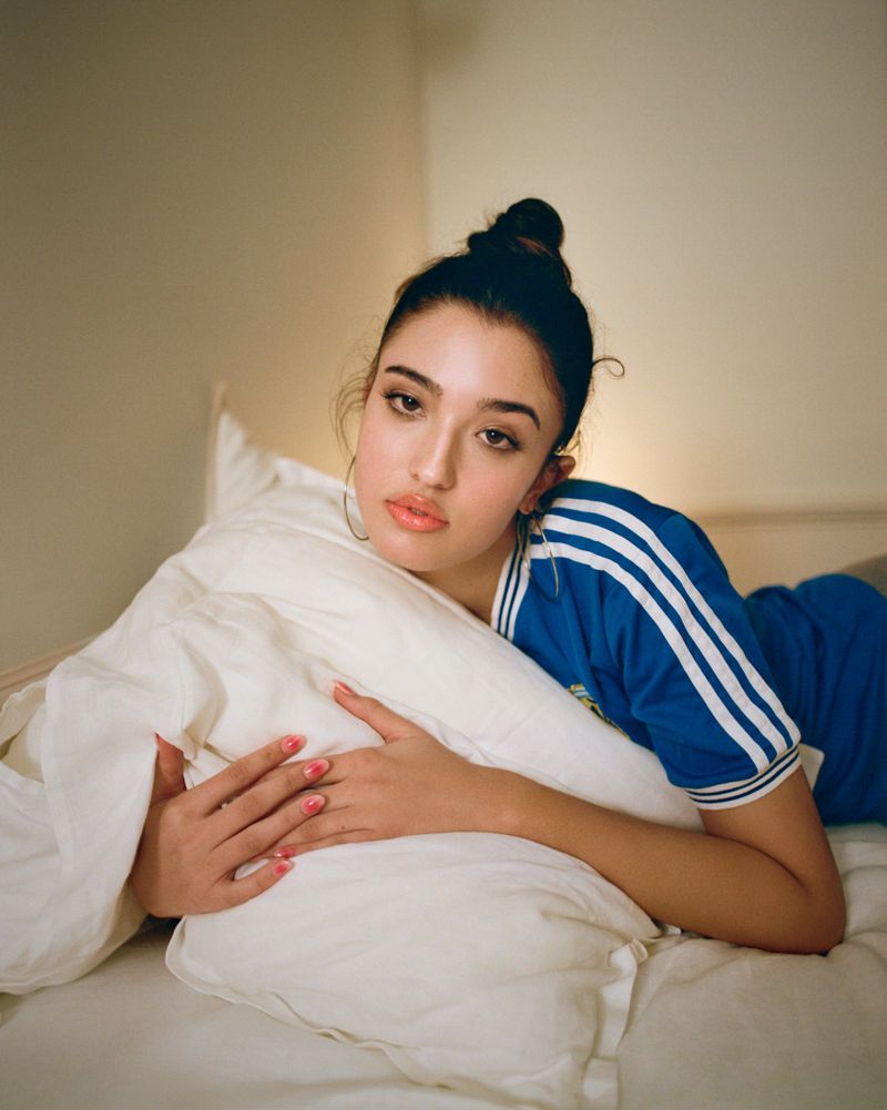 Young woman in a blue top hugging a white pillow on a bed in a softly lit bedroom setting