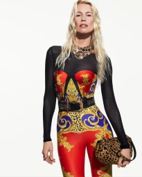 Claudia Schiffer modeling a Versace baroque print catsuit with a gold statement necklace and leopard print handbag against a white background