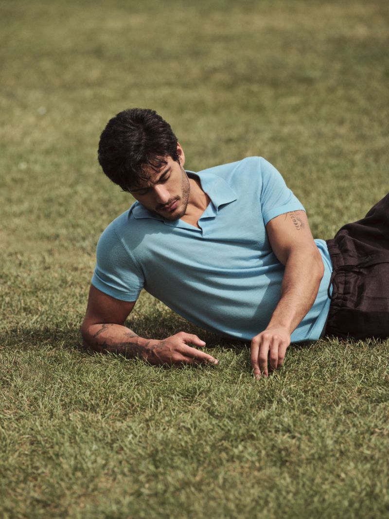 Ariyan Akaltun lying on a grassy lawn wearing a light blue polo shirt for BOSS by Beckham