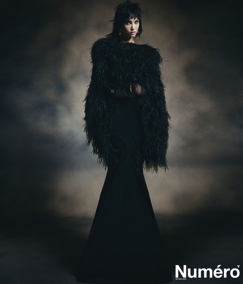 Adult woman in a dramatic full-length black gown with a feather boa in a dark, hazy studio environment for a fashion editorial.