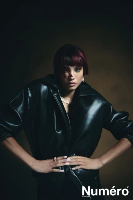Stylish portrait of a woman with dark hair and a burgundy fringe wearing a black leather jacket, set against a neutral backdrop.