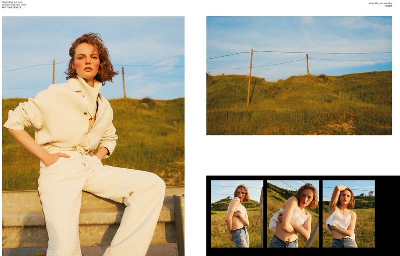 Model Fran Summers wearing a cream textured suit seated on a roadside guardrail against a sunlit grassy hill.