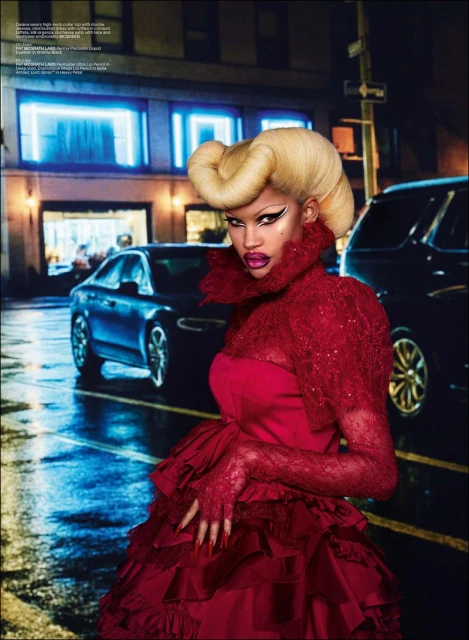 Elegant woman in a red gown with creative blonde updo poses in a city street setting at night, featuring car headlights and blurred details.