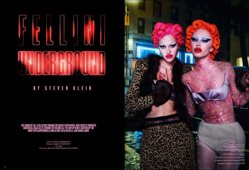 Two women with colorful hair and dramatic makeup pose in an urban setting. Fashion editorial with high contrast and street style.