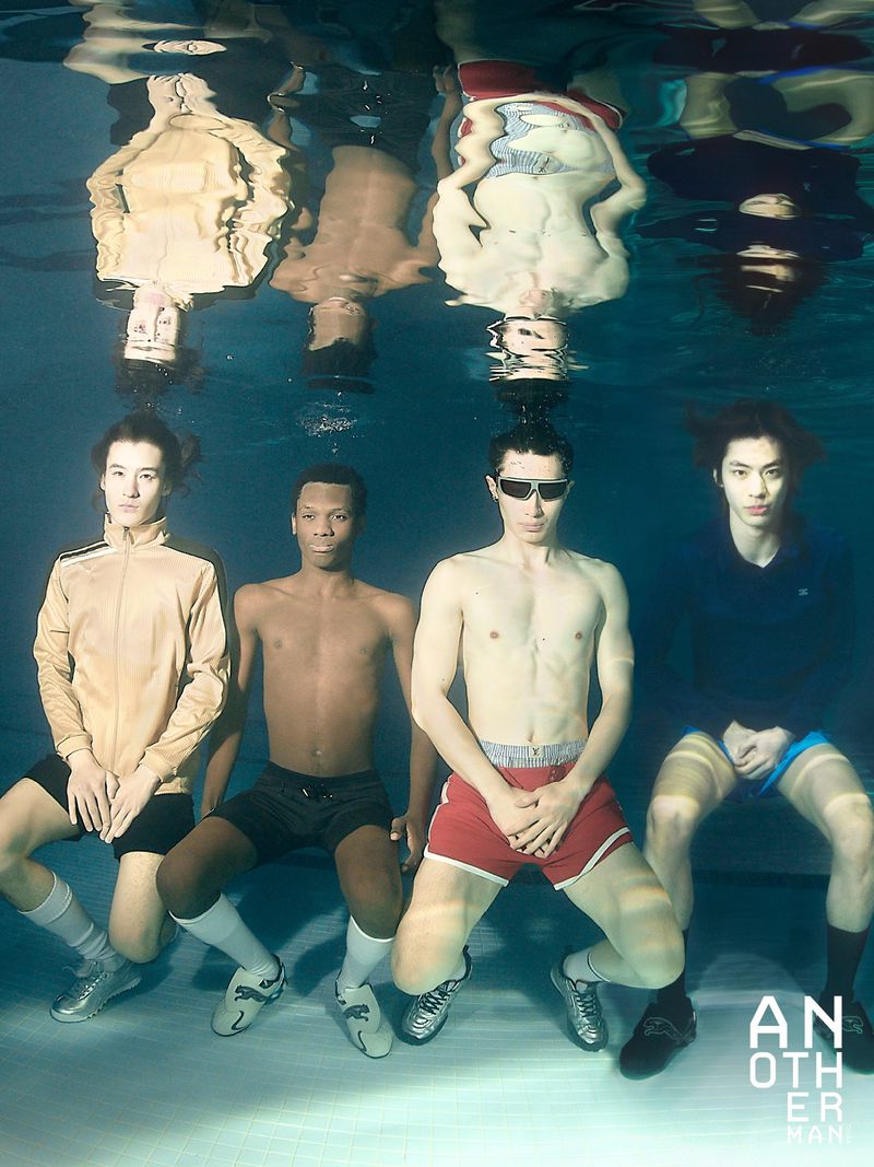 Four male models submerged underwater in a swimming pool, reflected on the surface above for an editorial fashion shoot.