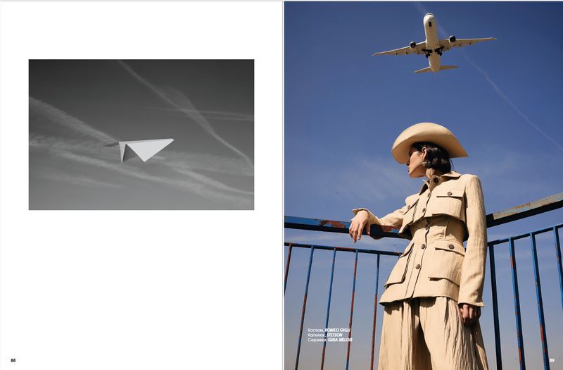 Model Rita Santos wearing a beige utility suit and wide-brim hat under a blue sky with an airplane flying overhead.