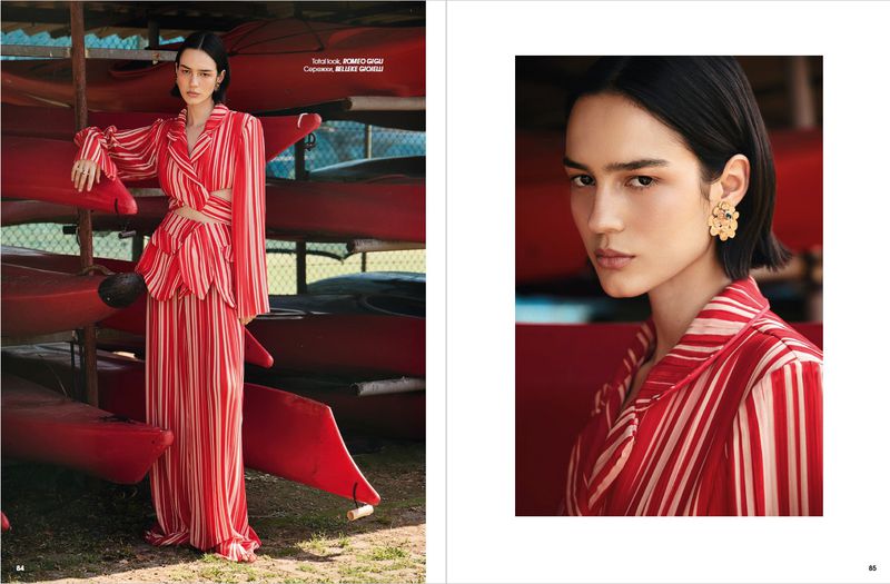 Model Rita Santos poses in a red and white striped two-piece set next to stacked red kayaks in an editorial magazine spread.