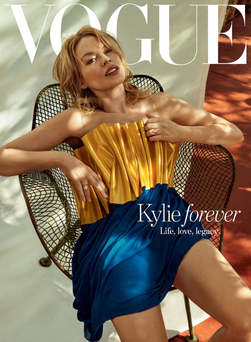 Magazine cover of Vogue Australia features a woman in a gold and blue dress sitting in a chair with Vogue logo and text overlay.