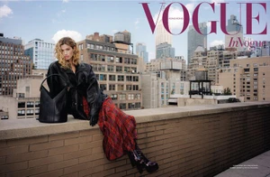 Model sitting on a brick rooftop ledge wearing a black leather jacket and plaid skirt against a city skyline