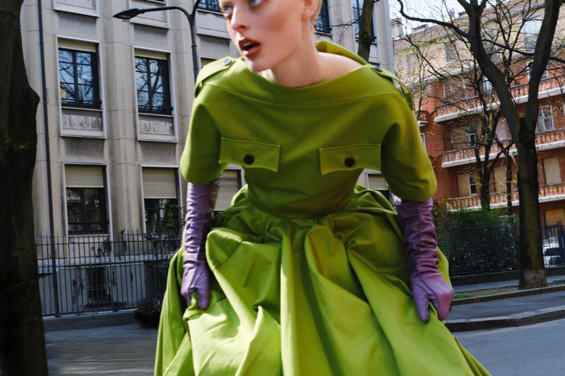 Model wearing a vibrant lime green structured dress and purple leather opera gloves outdoors on a city street.
