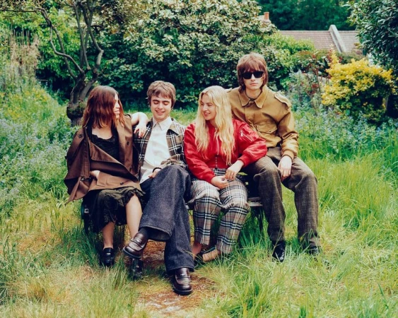 Four young adults are sitting on a bench in a grassy yard outside a home; group portrait featuring vintage-inspired casual fashion.