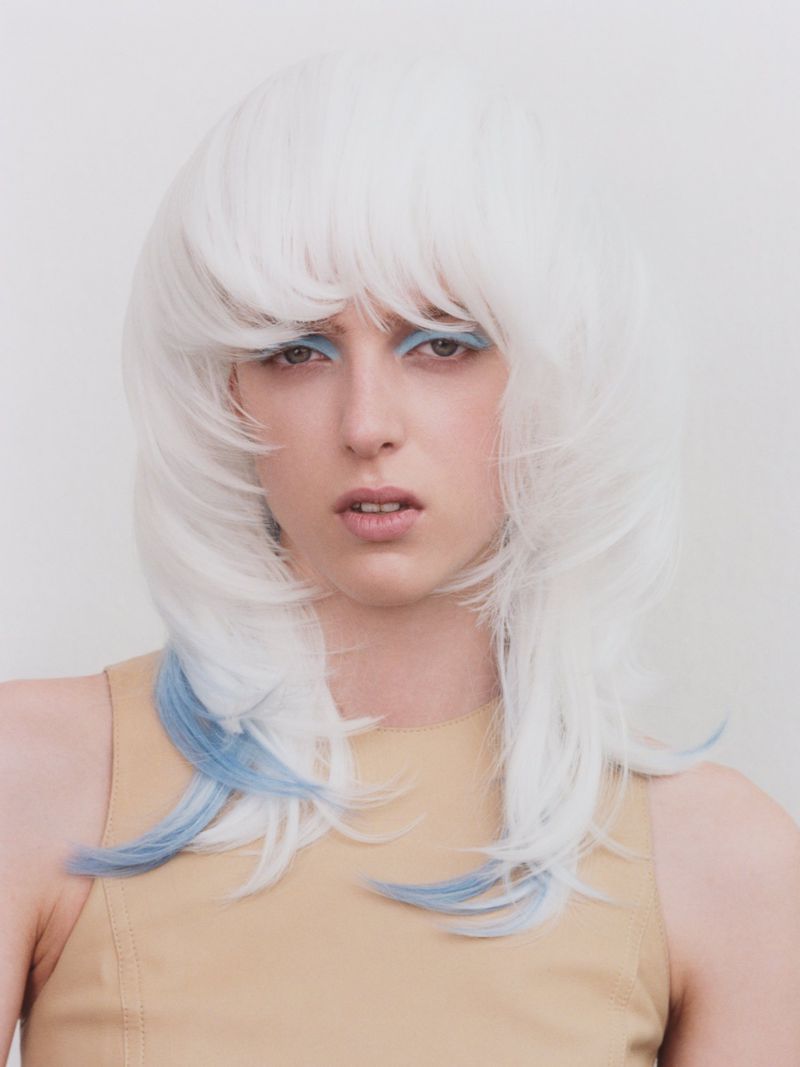 Model with white layered hair and blue highlights wearing a tan top against a neutral background