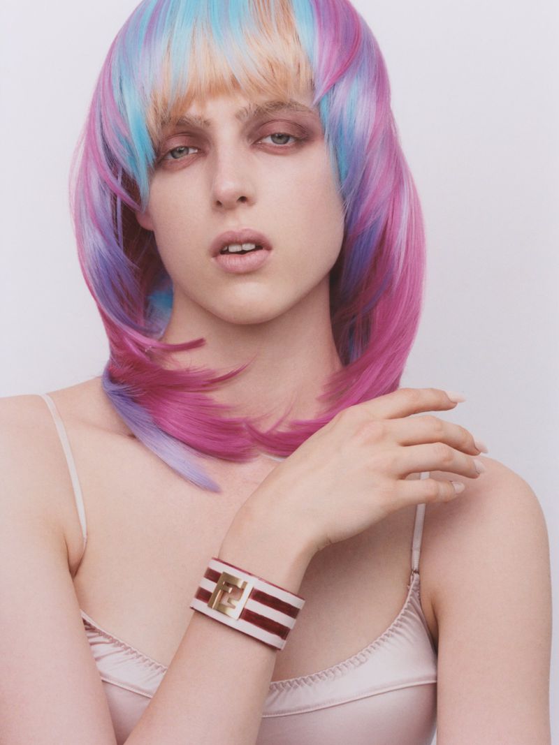 Model Amelia Anisiewicz with multicolored pastel hair wearing a striped cuff bracelet against a plain light studio backdrop.