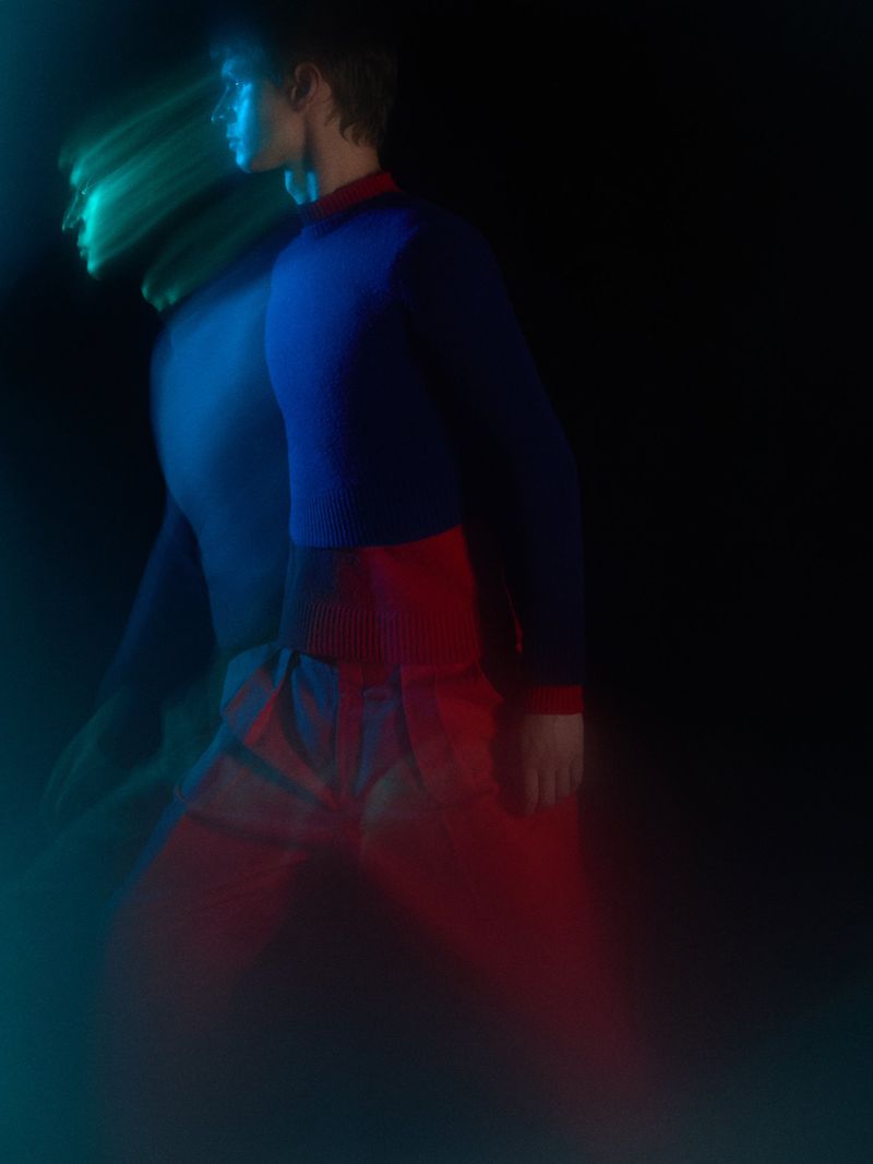 Model in motion with long exposure motion blur wearing a blue and red sweater against a dark background