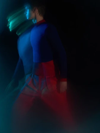 Model in motion with long exposure motion blur wearing a blue and red sweater against a dark background