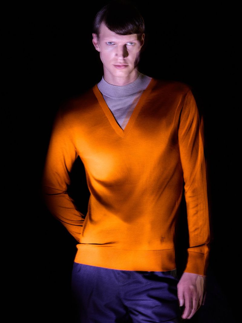 Male model in an orange v-neck sweater over a grey mock neck top against a black background for L'Officiel Hong Kong.