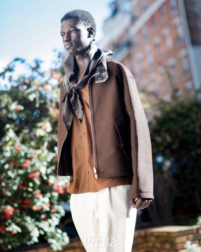 Model wearing a brown jacket and scarf outdoors with foliage in the background for Men's Uno International.