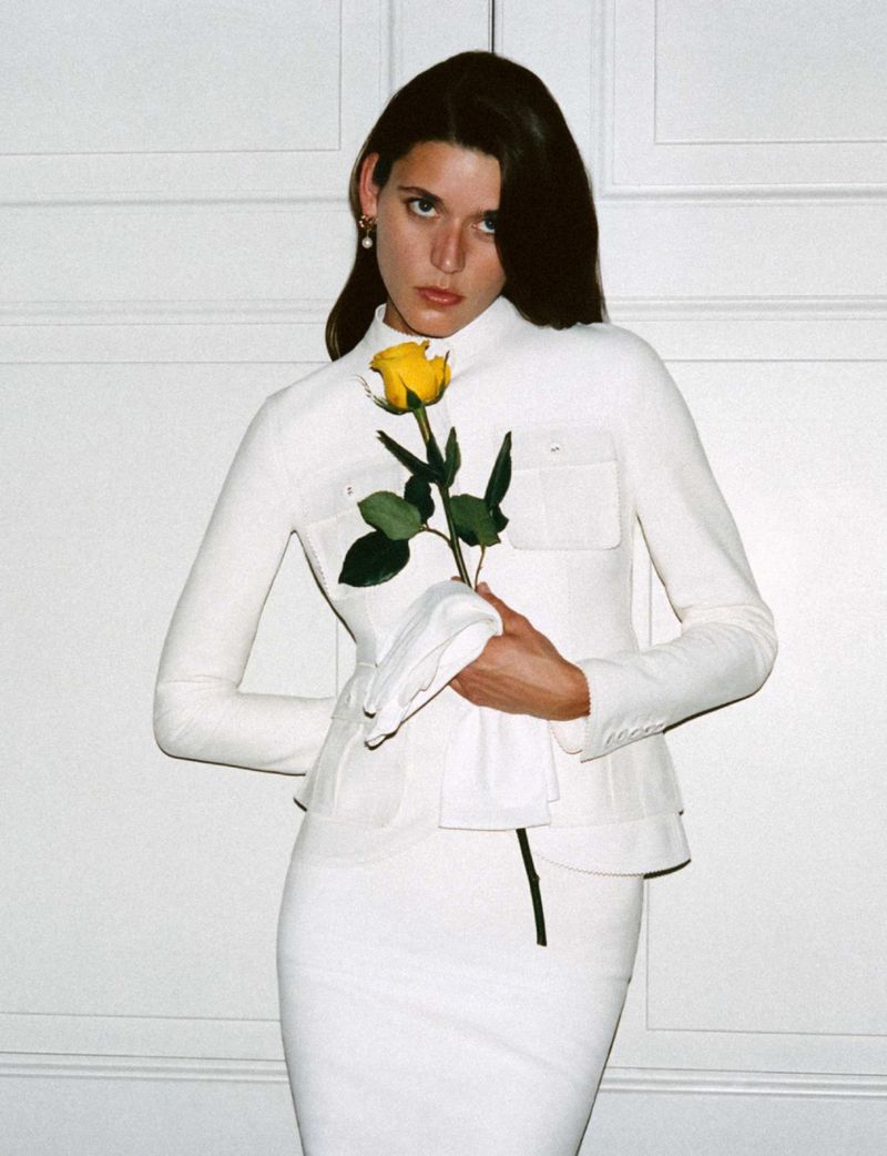 Model Vivienne Rohner in a white jacket holding a yellow rose against a panelled wall for Harper's Bazaar France