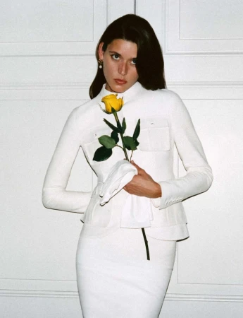 Model Vivienne Rohner in a white jacket holding a yellow rose against a panelled wall for Harper's Bazaar France