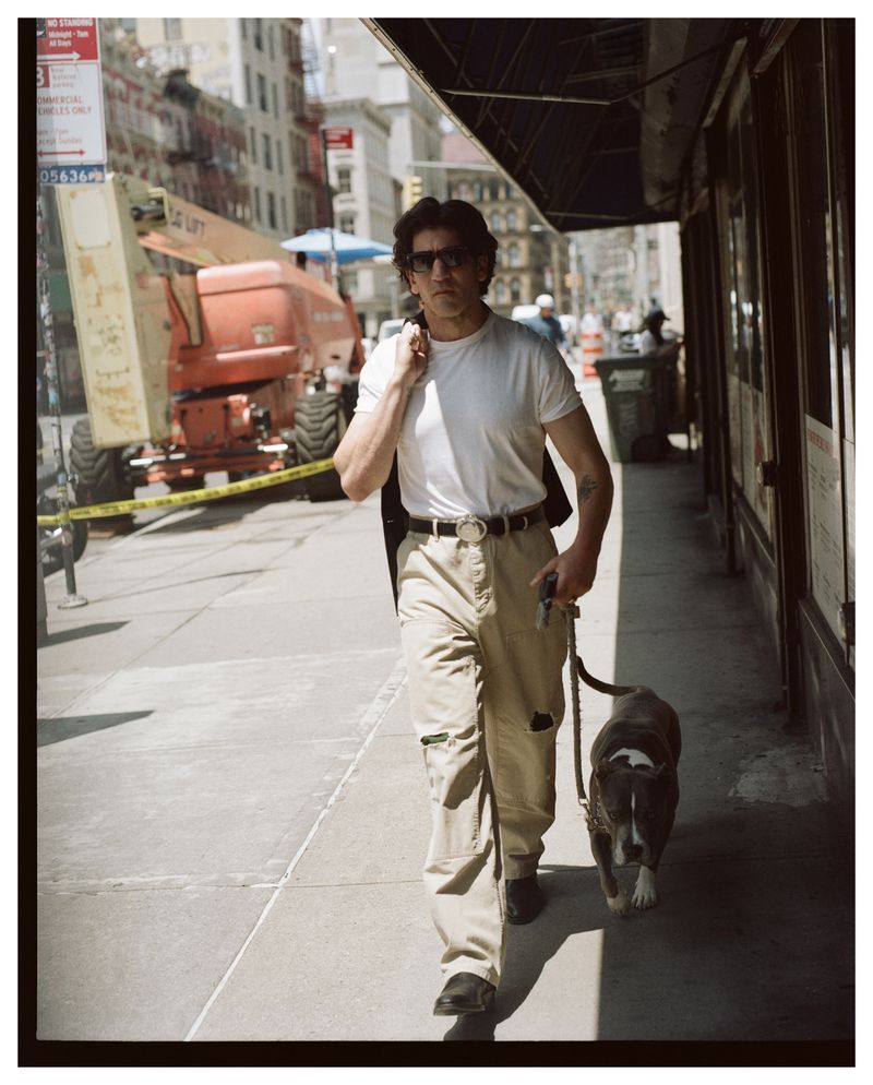 Jon Bernthal walking a dog on a city sidewalk wearing a white t-shirt and khaki pants for The Hollywood Reporter cover shoot