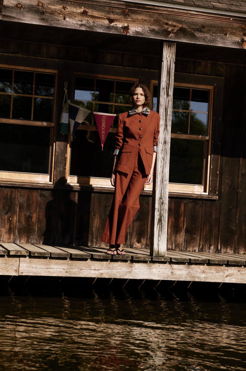Model Angel Galego wearing a rust-colored tailored suit on a wooden dock by the water for Veronica Beard.