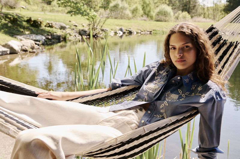 Model relaxing in a striped hammock by a serene lake for the Veronica Beard Pre-Fall campaign.