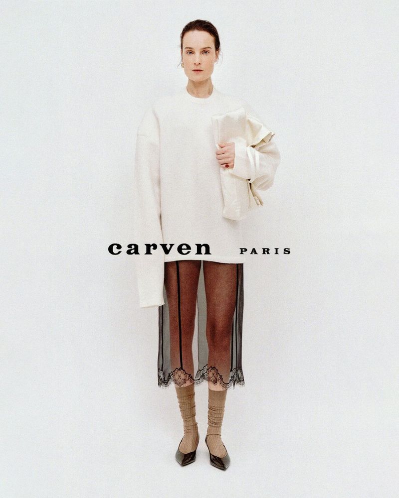 Charlotte Tomas in an oversized off-white sweater and sheer black lace skirt against a plain white studio background.