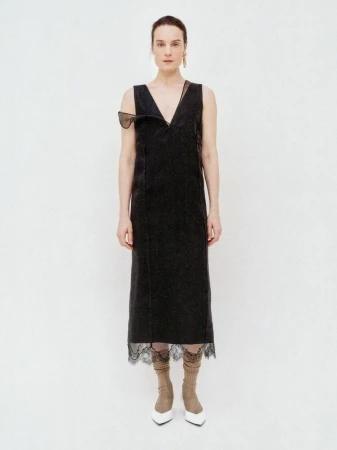 Model Charlotte Tomas poses in a black sleeveless V-neck midi dress with lace hem trim and white pointed heels on a white backdrop.