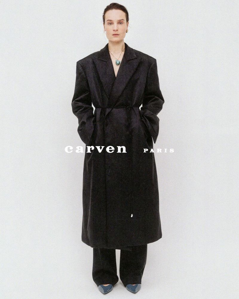 Model in a long black belted coat and trousers against a white seamless background with Carven Paris branding.