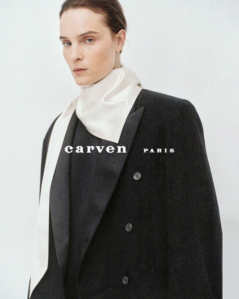 Model Charlotte Tomas wearing a tailored black double-breasted blazer and cream silk neck scarf for Carven.