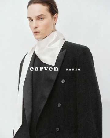 Model Charlotte Tomas wearing a tailored black double-breasted blazer and cream silk neck scarf for Carven.
