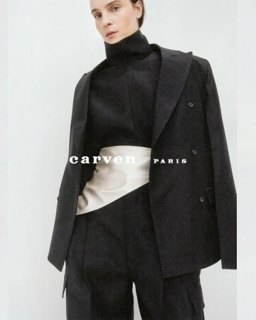 Model wearing a black tailored blazer, turtleneck top, and an ivory satin waist sash against a neutral backdrop.