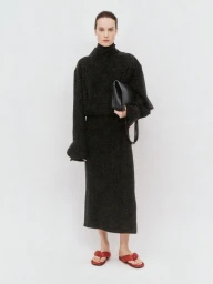Model Charlotte Tomas wearing a black turtleneck midi dress with a black clutch and red sandals against a white background.