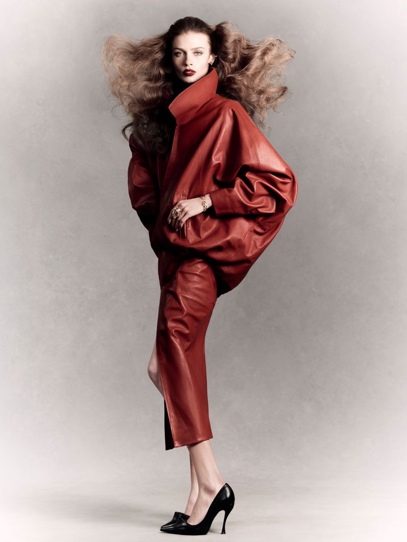 Model Ella McCutcheon in an oversized red leather coat and matching skirt posing against a grey studio backdrop.