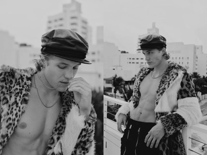 Monochrome fashion shots of a blond male model wearing a leopard print coat and black sailor cap, posing against a city backdrop.