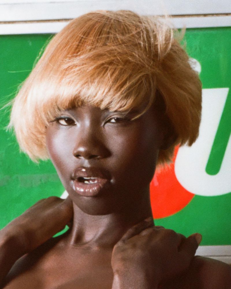 Close-up of a black woman with short blonde hair posing in front of a green background, showcasing a striking contrast and elegant style.