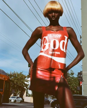 Model wearing a red printed top and skirt with blonde bob wig standing outdoors against power lines