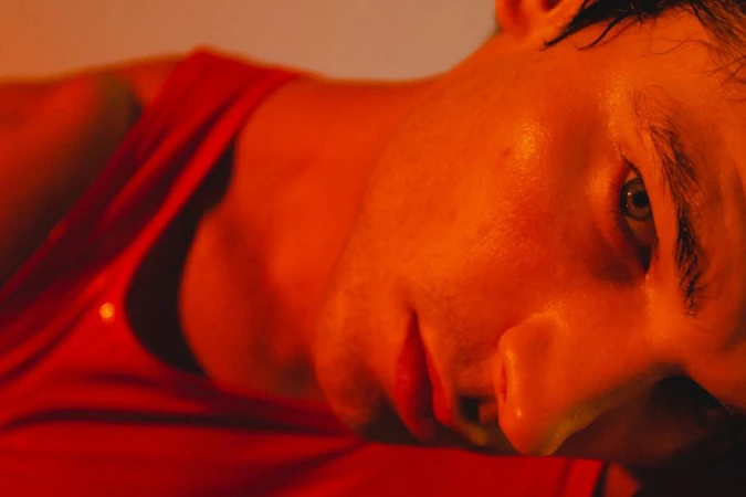 Close-up portrait of a male model wearing a red tank top under warm orange lighting for Numero Netherlands.
