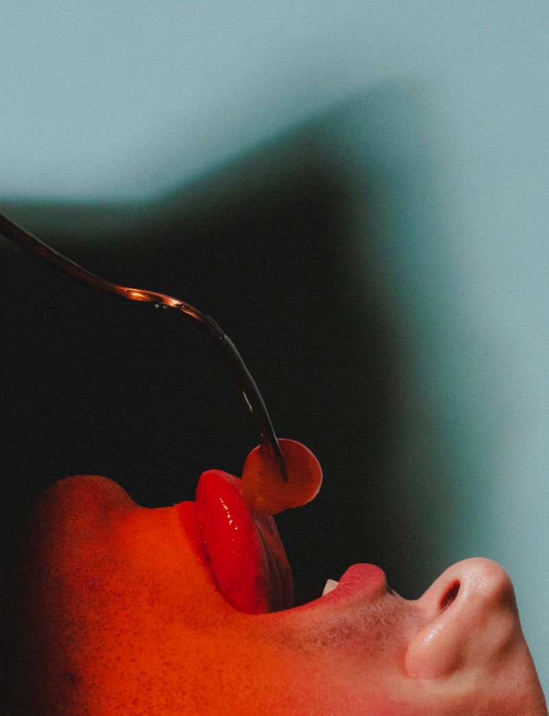 Close-up profile of model Stefano Tomadini with mouth open catching a translucent food sphere on a metal fork in red lighting.