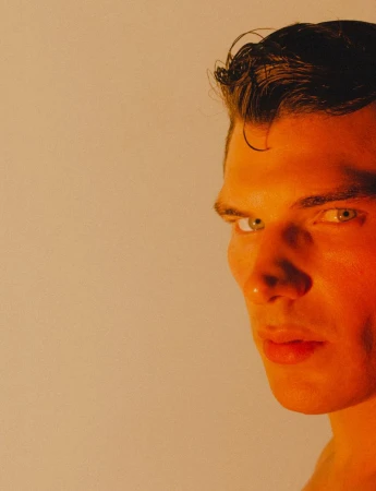 Close-up portrait of a man under warm amber lighting against a plain background for Numero Netherlands.