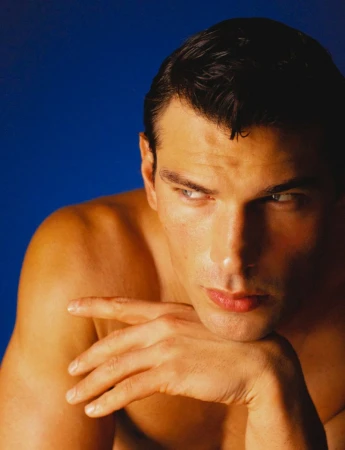 Close-up portrait of model Stefano Tomadini resting his chin on his hand against a deep blue background.