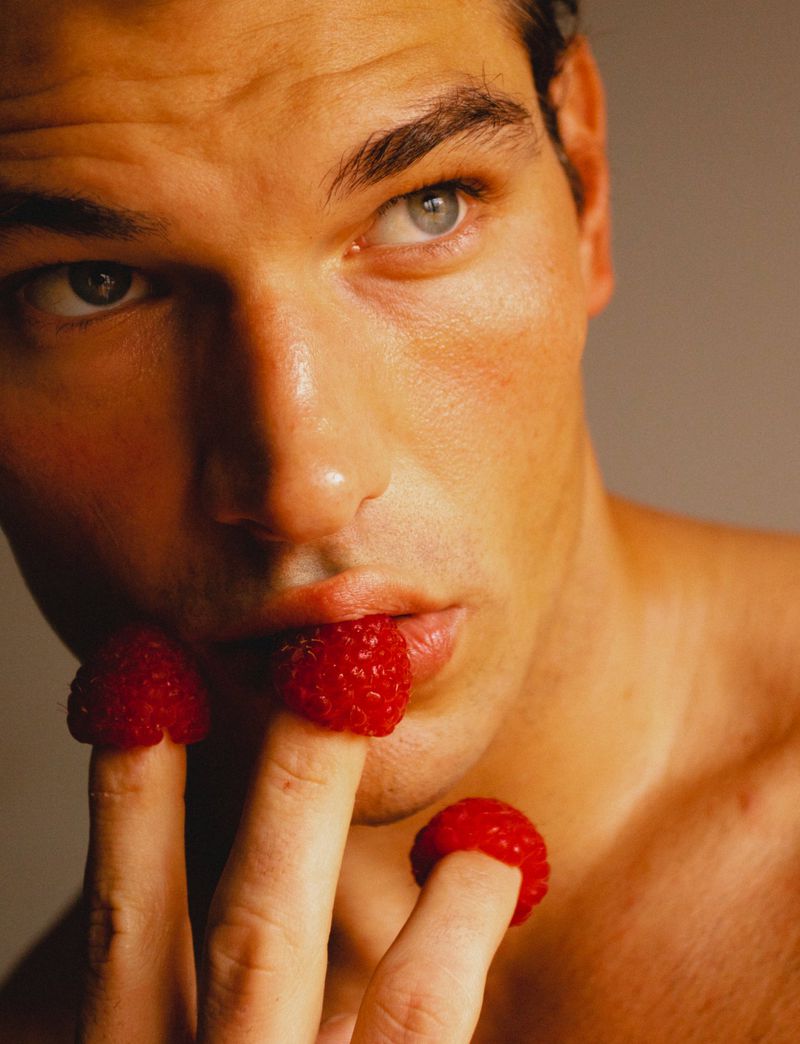 Close-up portrait of a male model with raspberries balanced on his fingertips for Numero Netherlands Shifting Colours